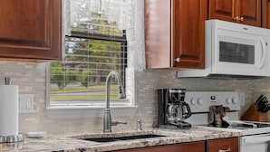 A kitchen with a granite countertop, wooden cabinets, a stainless steel sink, a microwave, and a coffee maker.