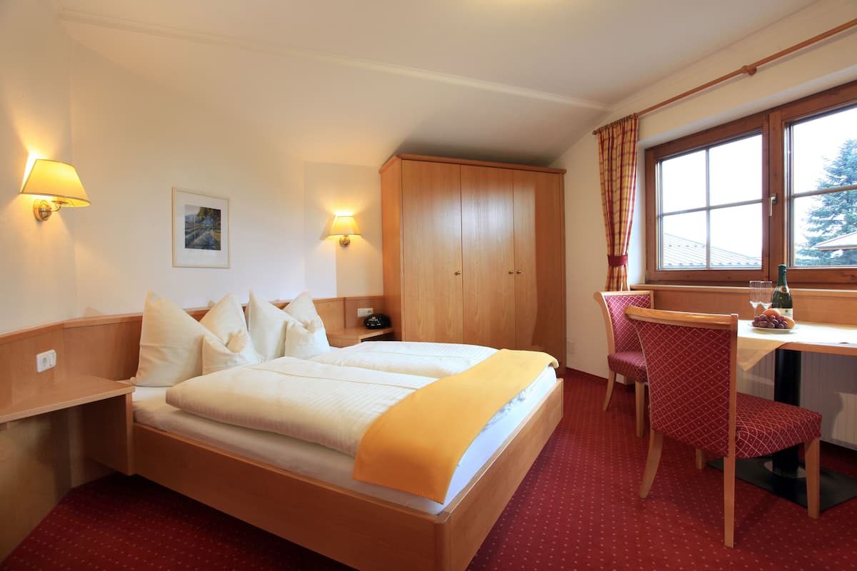 Habitación de hotel con cama doble, escritorio, silla, armario y ventana con cortinas.