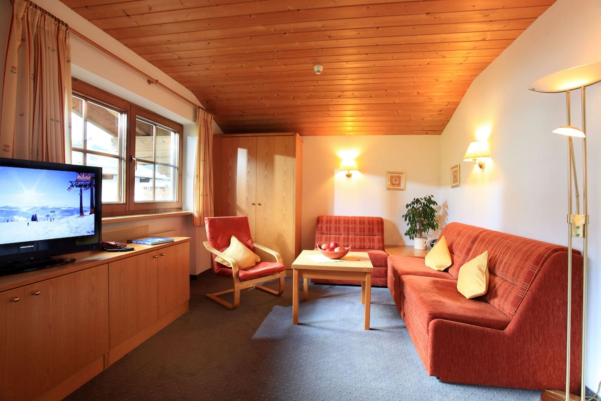 Una sala de estar acogedora con televisor, muebles de madera y una ventana con cortinas.