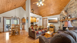 A spacious living area with a wooden ceiling, a stone wall, a fireplace, and a cozy seating arrangement. - Dakota Lodge 2 Bedroom Home by RedAwning (Branson West)