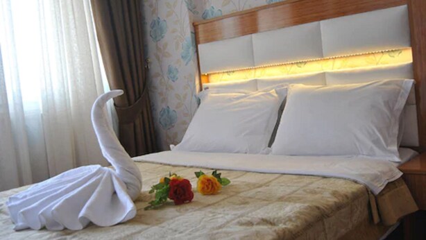 A neatly made bed with white linens, a wooden headboard, and a decorative swan pillow. - Hotel Star Park (Istanbul)