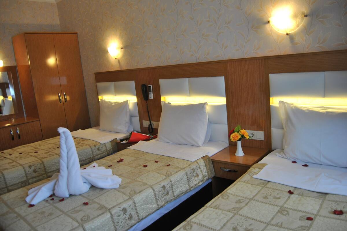 A hotel room with two beds, a wooden wardrobe, a bedside telephone, and a vase with flowers.