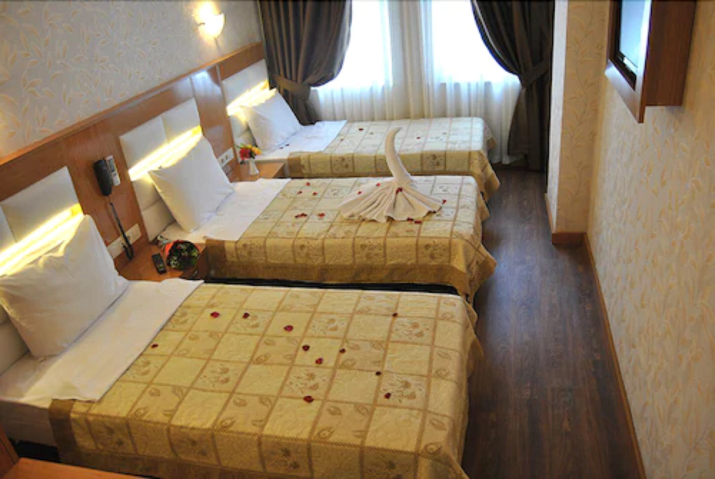A hotel room with two beds, each with a floral bedspread and a decorative towel. There are bedside tables with lamps and a clock.