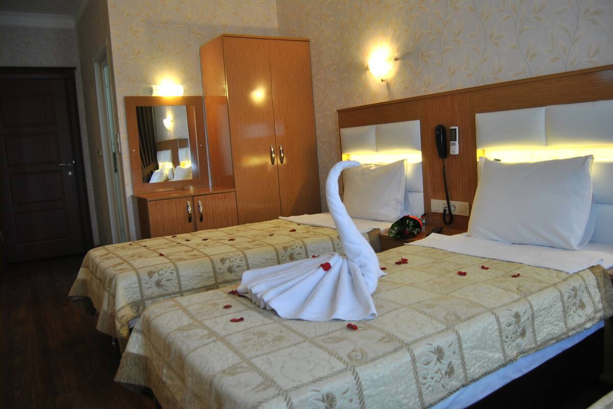 A hotel room with two beds, a wooden wardrobe, a mirror, a bedside telephone, and a wall-mounted light fixture.