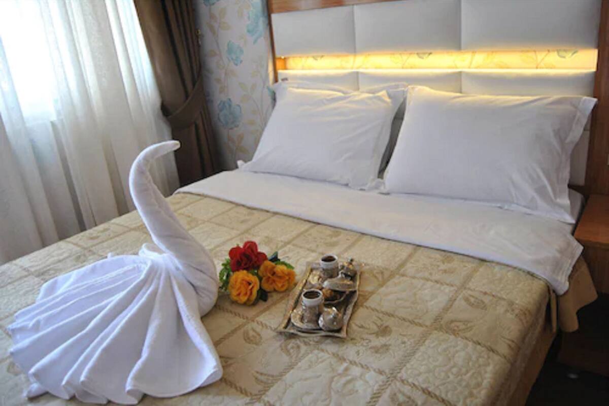 A neatly made bed with white linens, a tray with tea cups, and a decorative swan towel.