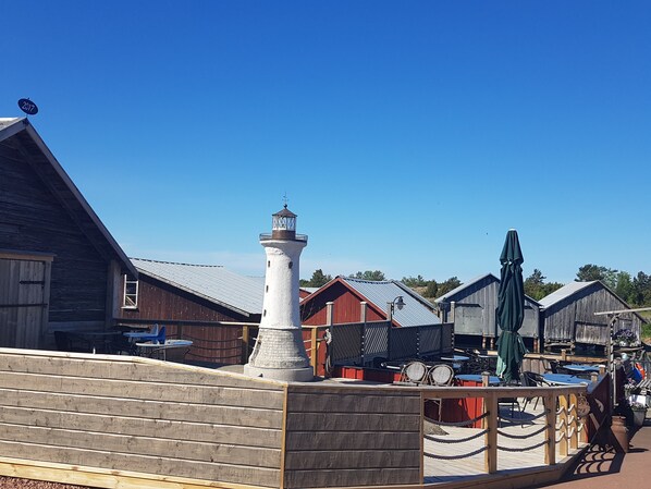 A waterfront property with a prominent white lighthouse, wooden buildings, and outdoor seating areas.