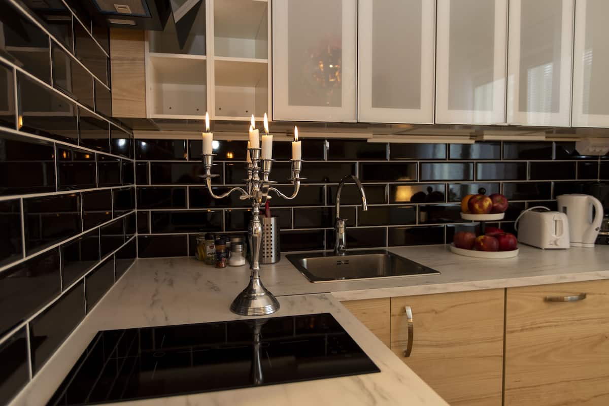 A modern kitchen with black and white tiles, a built-in stove, a sink, and a fruit bowl on the counter.