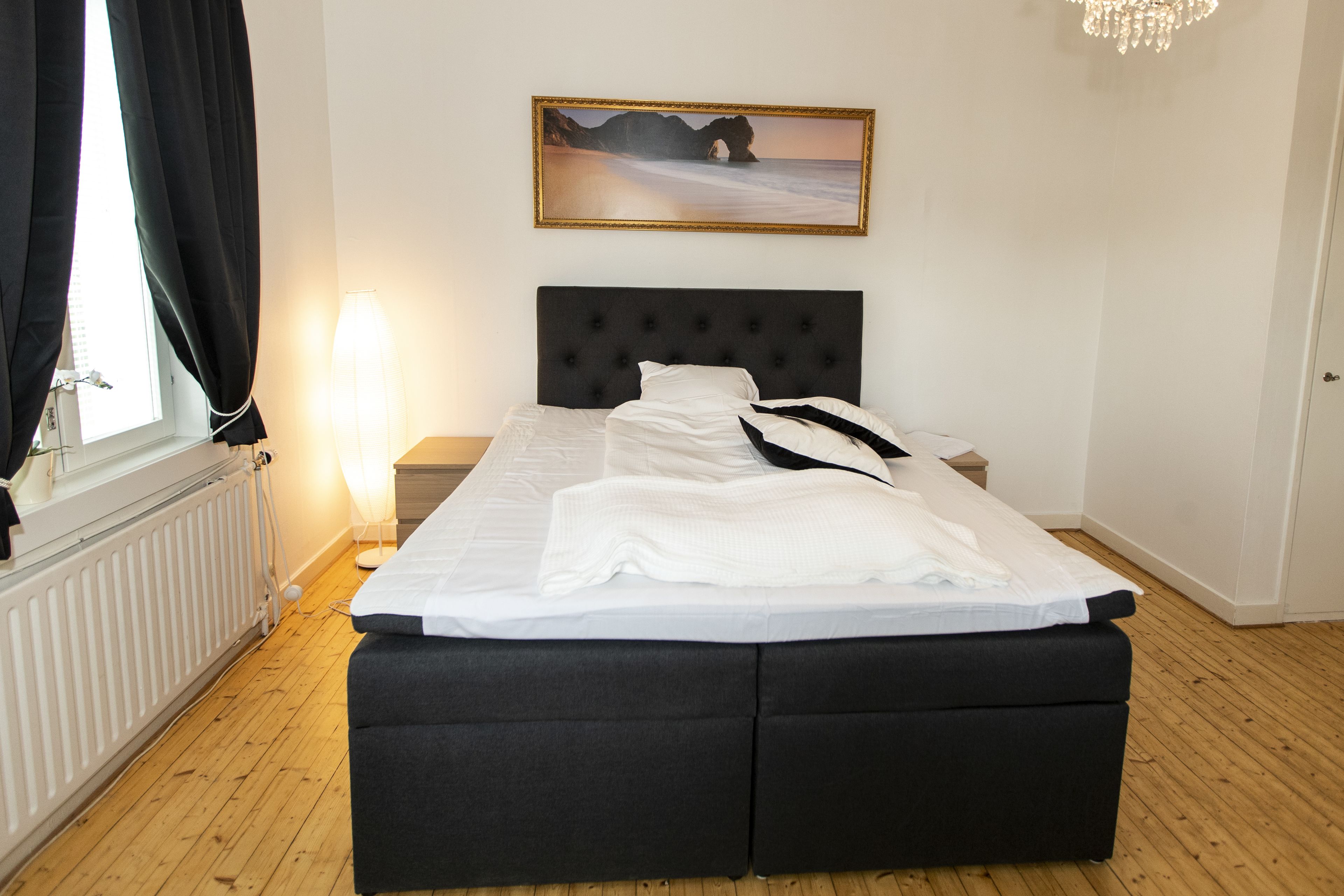 A neatly made bed with a black headboard, a bedside table with a lamp, and a framed picture on the wall.