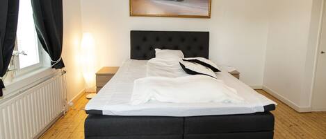 A neatly made bed with a black headboard, a bedside table with a lamp, and a framed picture on the wall.