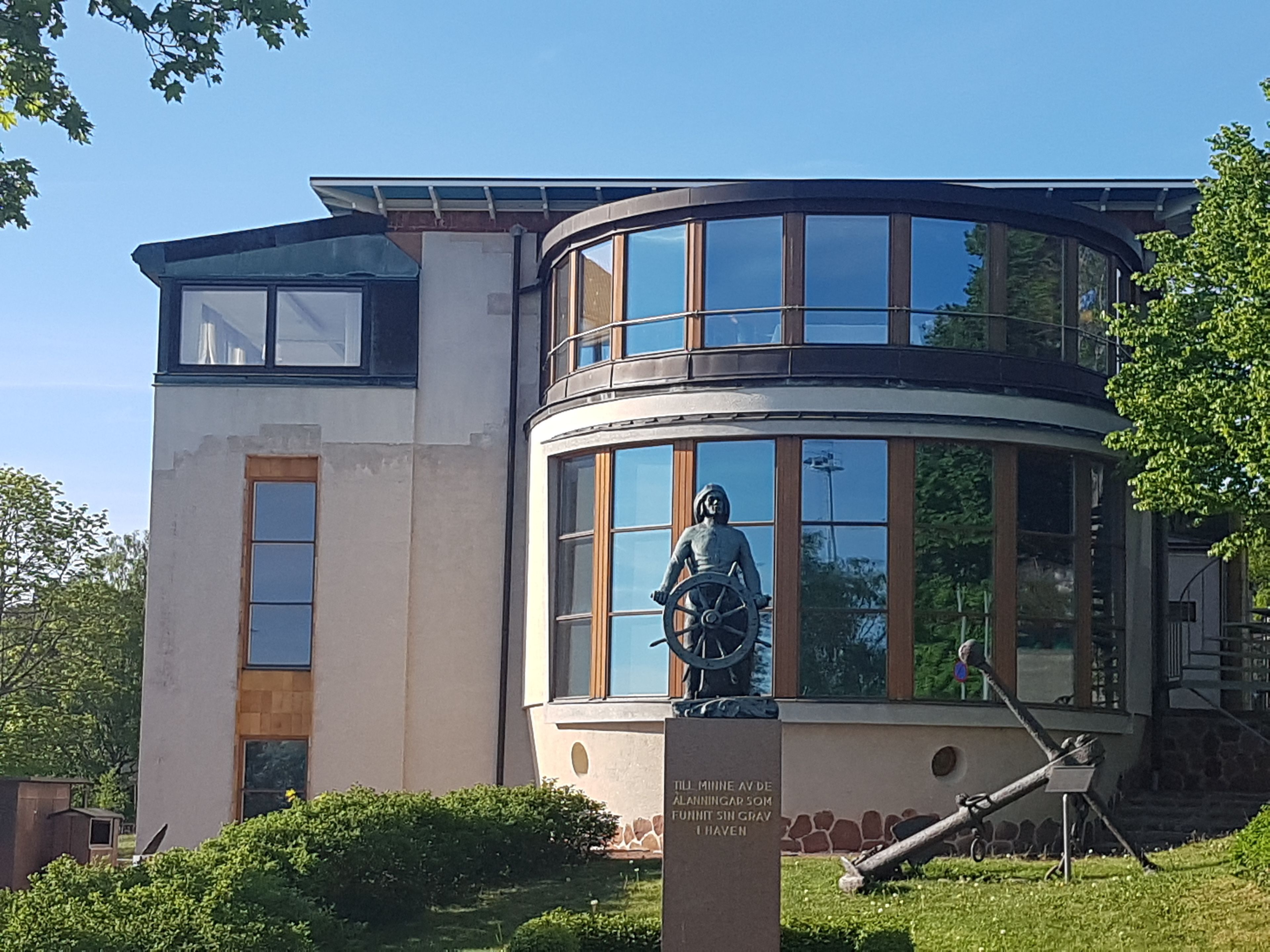 Ein Gebäude mit einer Statue einer Person, die ein Rad hält, einer Tafel mit Text und einer gewölbten Glasstruktur.