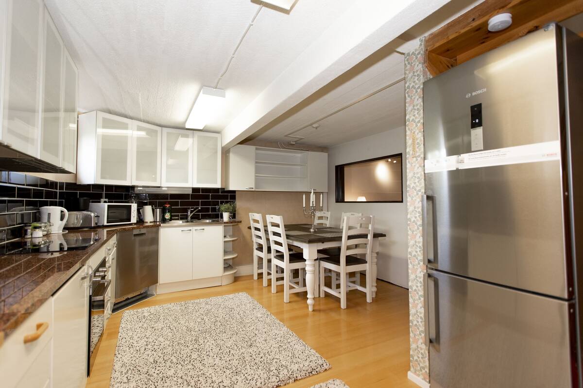 A modern kitchen with white cabinets, a stainless steel refrigerator, and a dining area with a wooden table and chairs.