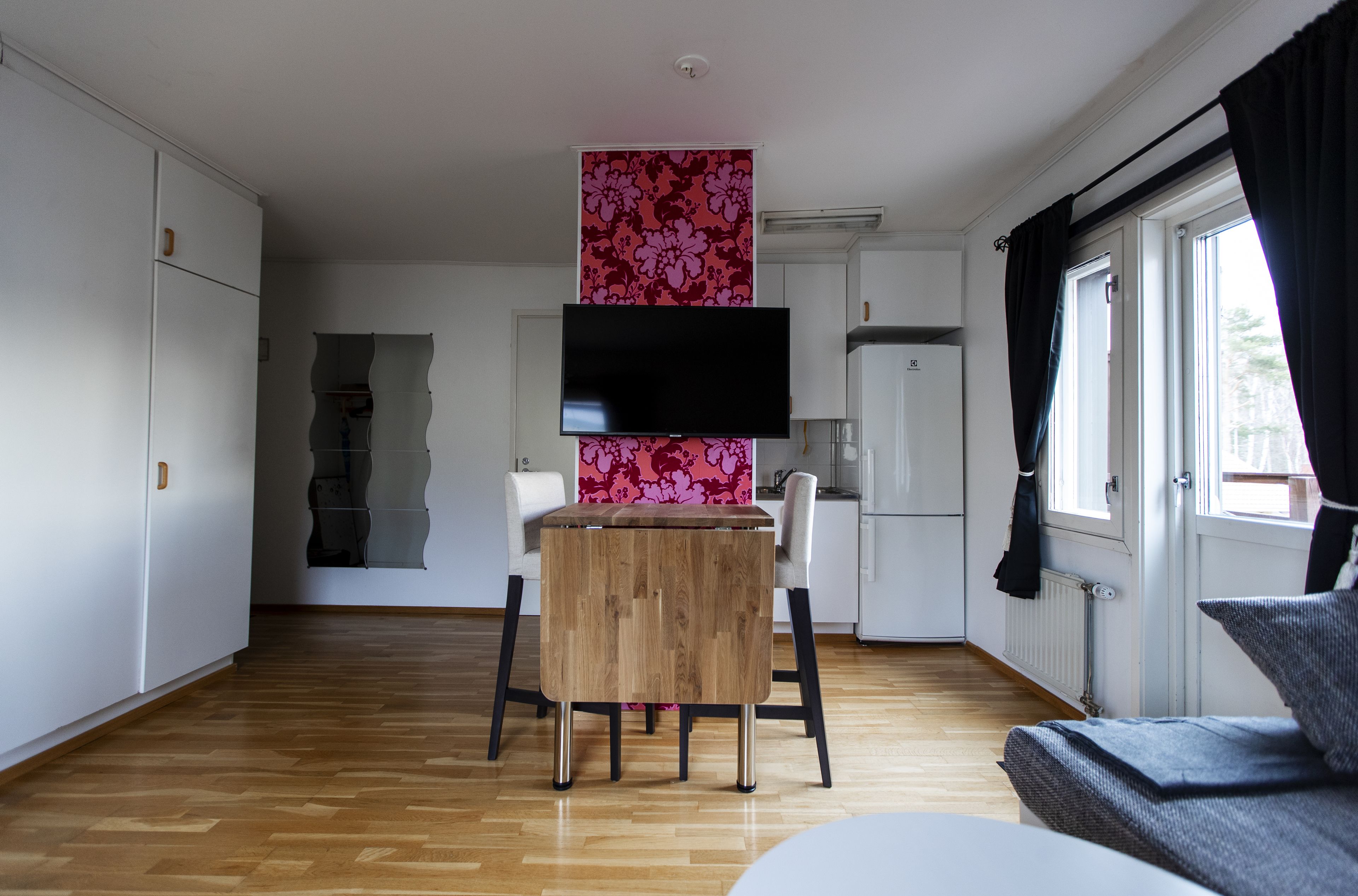 Une cuisine moderne avec une table en bois, des armoires blanches, un téléviseur à écran plat et une fenêtre avec des rideaux.
