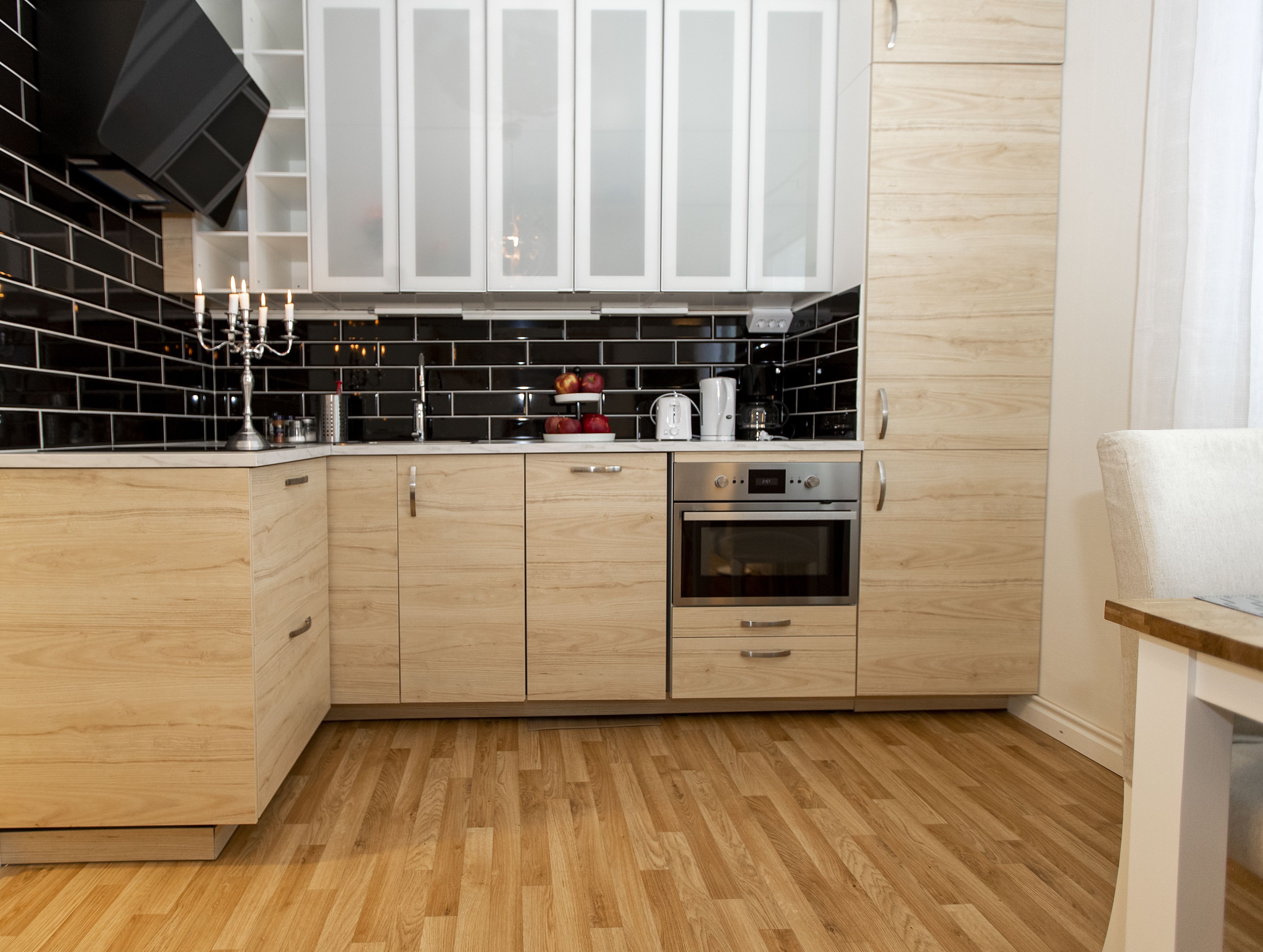 A modern kitchen with wooden cabinets, a black tiled backsplash, and a stainless steel oven.