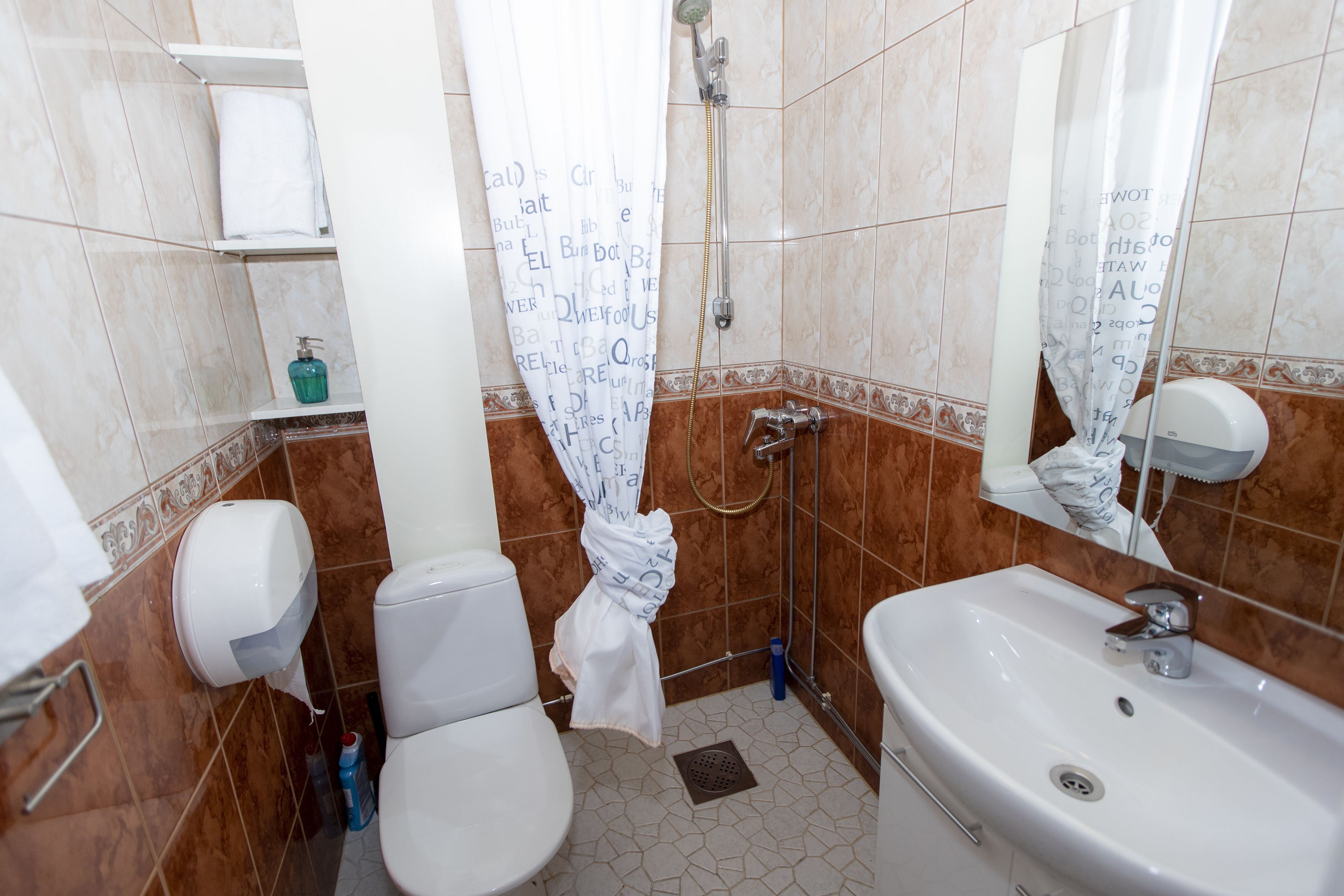 Un baño con inodoro, lavamanos, ducha y dispensador de toallas.