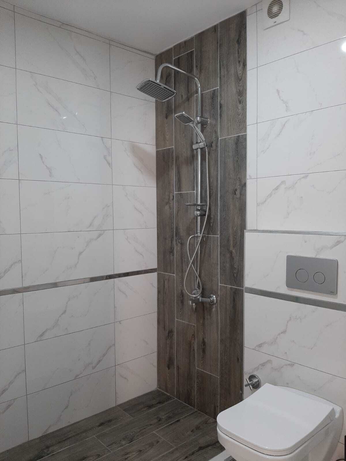 A modern bathroom with a shower, toilet, and marble tiles.