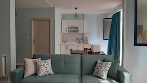 Una sala moderna con un sofá verde, una mesa de comedor y una zona de cocina con armarios blancos.