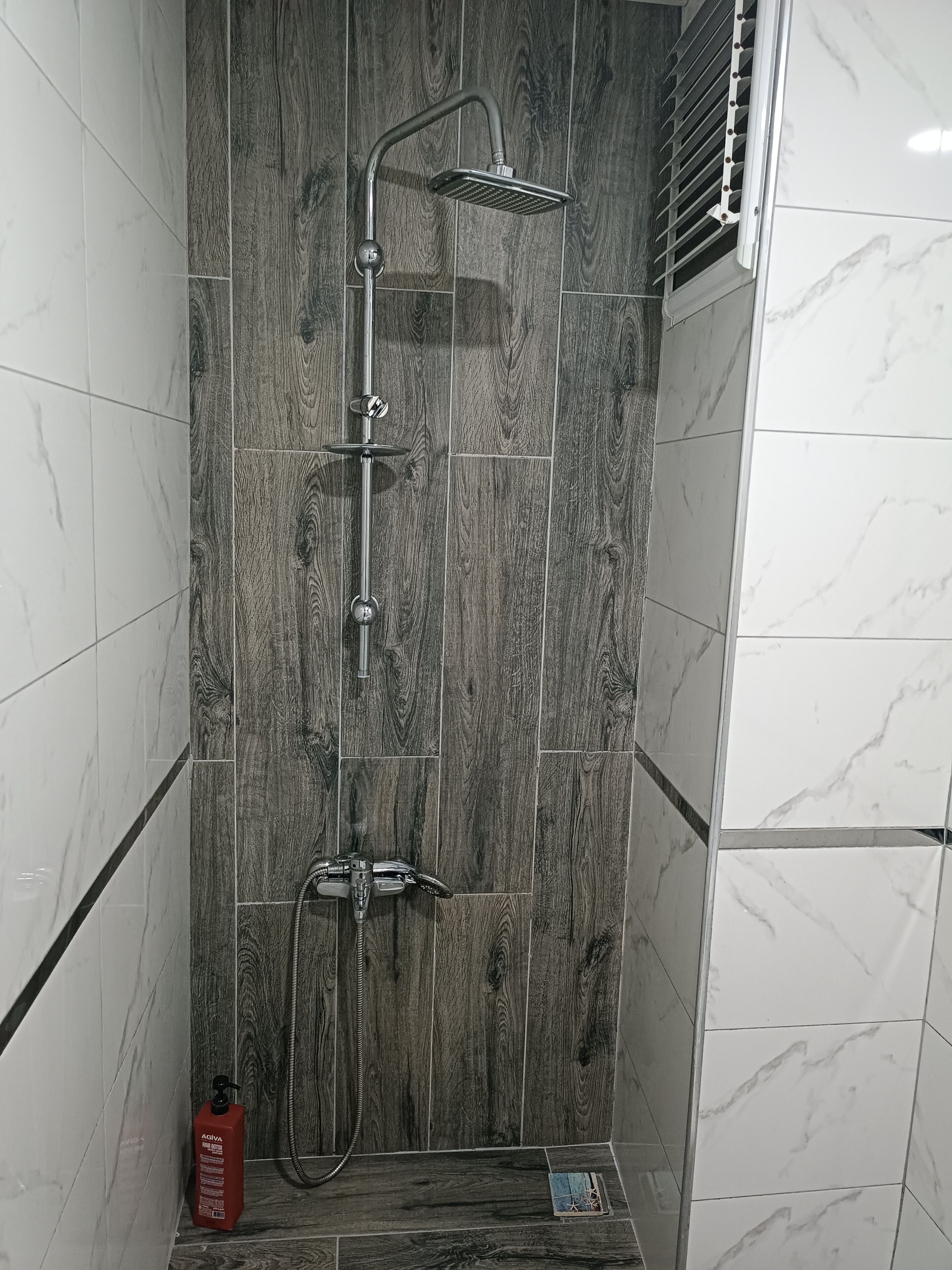 Una doccia con parete rivestita in legno, un soffione a mano, un soffione a parete e un tubo flessibile per doccetta.