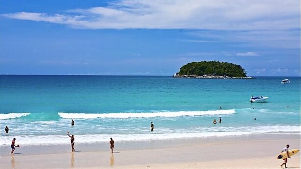 A beach with people, a boat, and a small island in the distance. - Kata Plaza 1 bedroom Centrical Apartment (Karon)