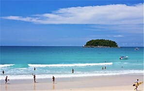 A beach with people, a boat, and a small island in the distance. - Kata Plaza 1 bedroom Centrical Apartment (Karon)