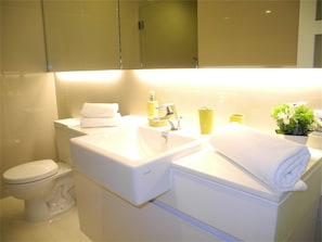 A modern bathroom with a white sink, toilet, and a mirror above the sink. There are towels and a small plant on the counter. - Kata Plaza 1 bedroom Centrical Apartment (Karon)