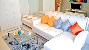 A modern living room with a white sofa, glass coffee table, and a flat-screen TV.
