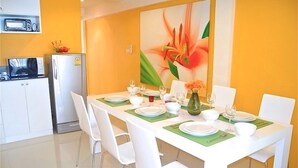 A dining area with a white table set for four, surrounded by white chairs. A painting of a flower is on the wall behind the table.