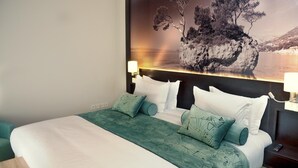 Hotellihuone, jossa on suuri sänky, näköala kallioiselle saarelle ja yöpöytä, jossa on lamppu.