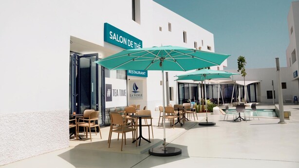 Ulkoterassi, jossa on pöytiä ja tuoleja, uima-allas sekä kyltit, joissa lukee ”Salon de Thé” ja ”La Voile Restaurant”.