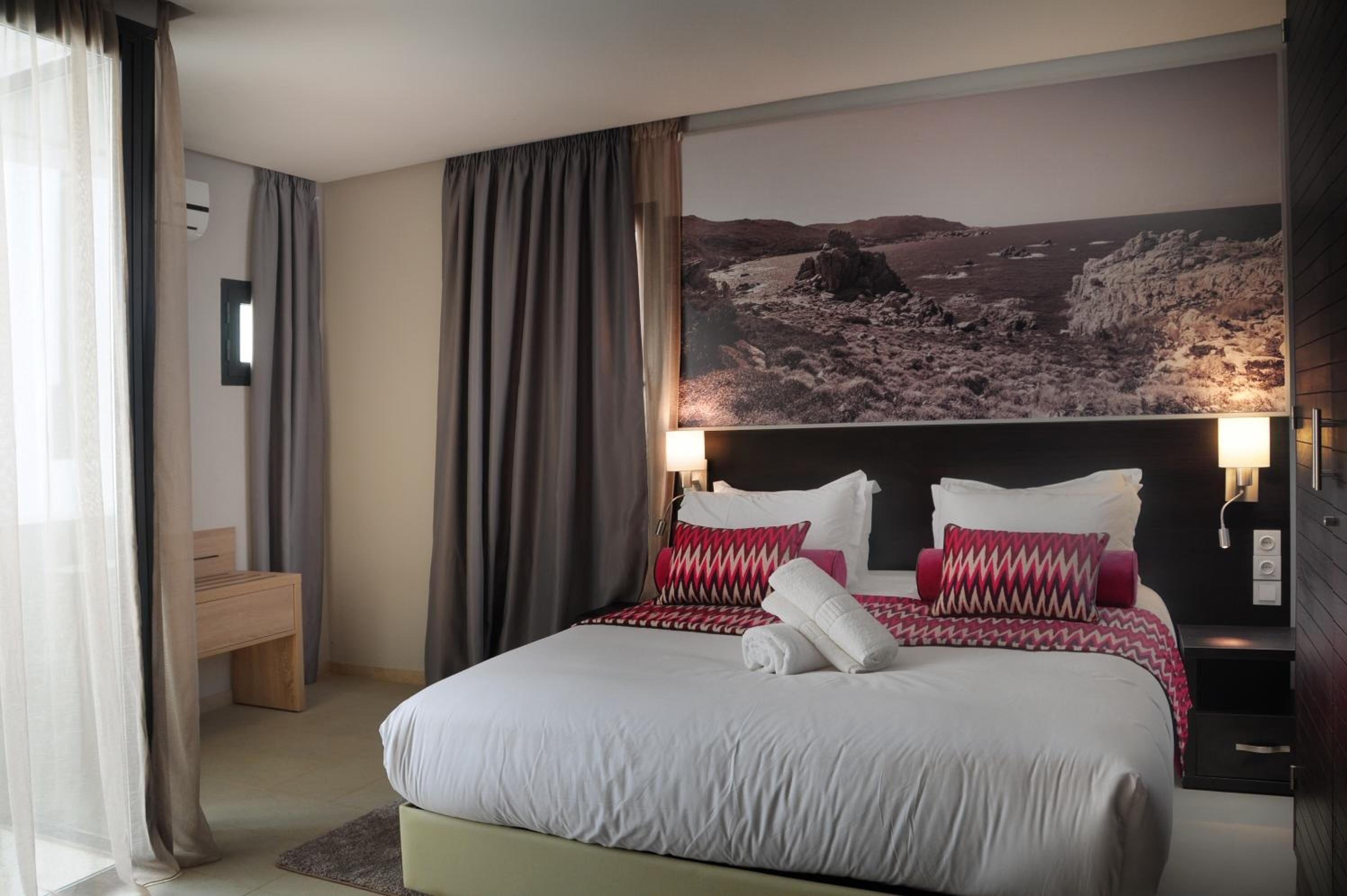 A modern hotel room with a large bed, a desk, and a scenic wall mural.
