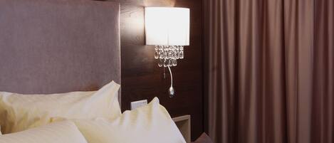 Una habitación de hotel con una cama bien hecha, una lámpara de pared y una cortina.