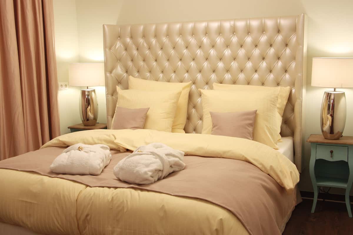 A neatly made bed with a tufted headboard, two bedside tables with lamps, and a pair of towels on the bed.