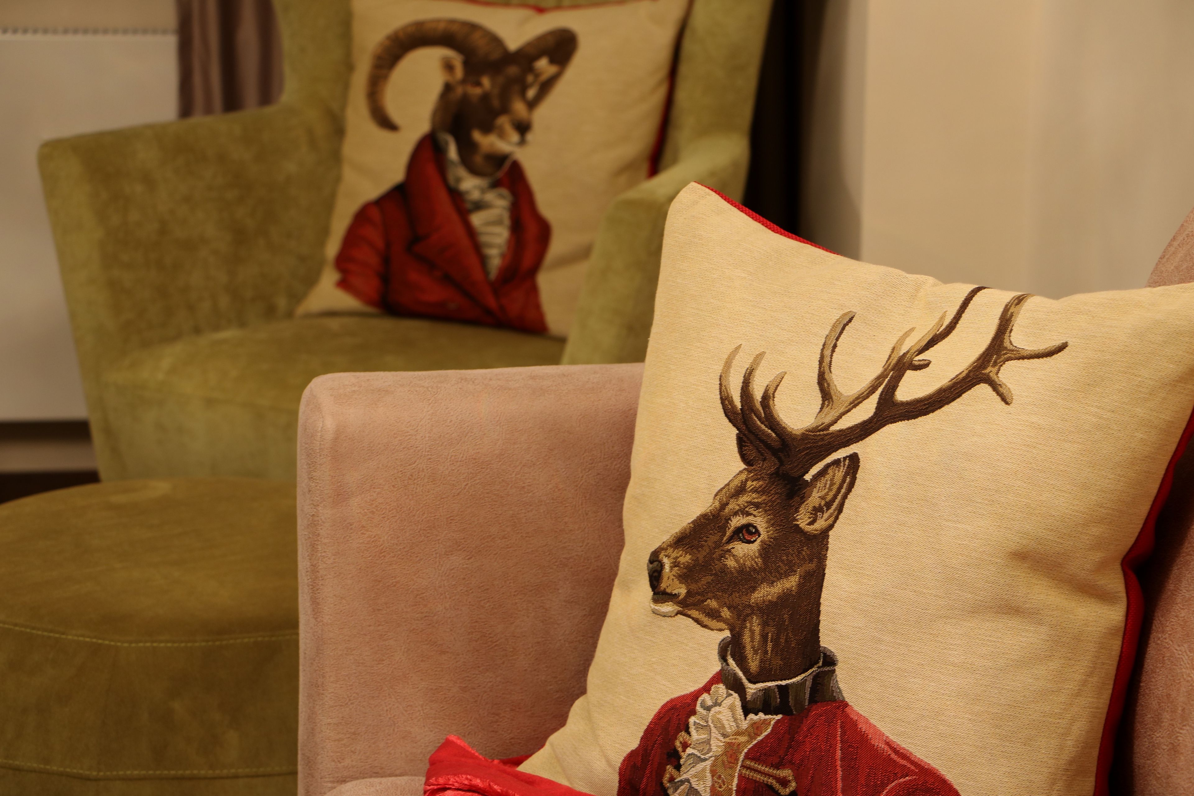 A room with two armchairs, one with a cushion featuring a deer in a red outfit and another with a cushion featuring a fox in a red outfit.