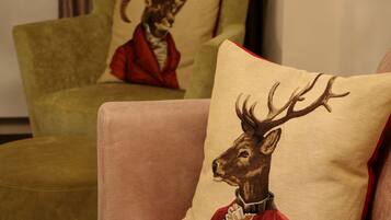 A room with two armchairs, one with a cushion featuring a deer in a red outfit and another with a cushion featuring a fox in a red outfit.