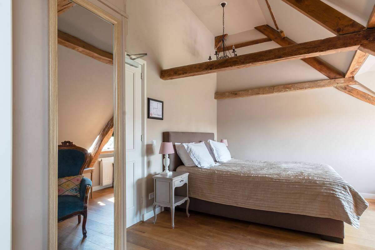 A bedroom with a sloped ceiling, a bed with a headboard, a nightstand, a chair, and a lamp.