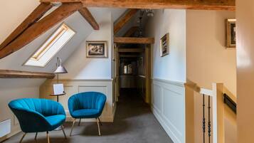 Un couloir étroit avec des poutres en bois, une lucarne et deux chaises bleues.