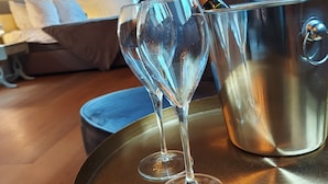 A room with a wooden floor, a bed with white bedding, a blue cushion, and a metal bucket with two glasses and a bottle of champagne. - Abbey Abcoude (Abcoude)