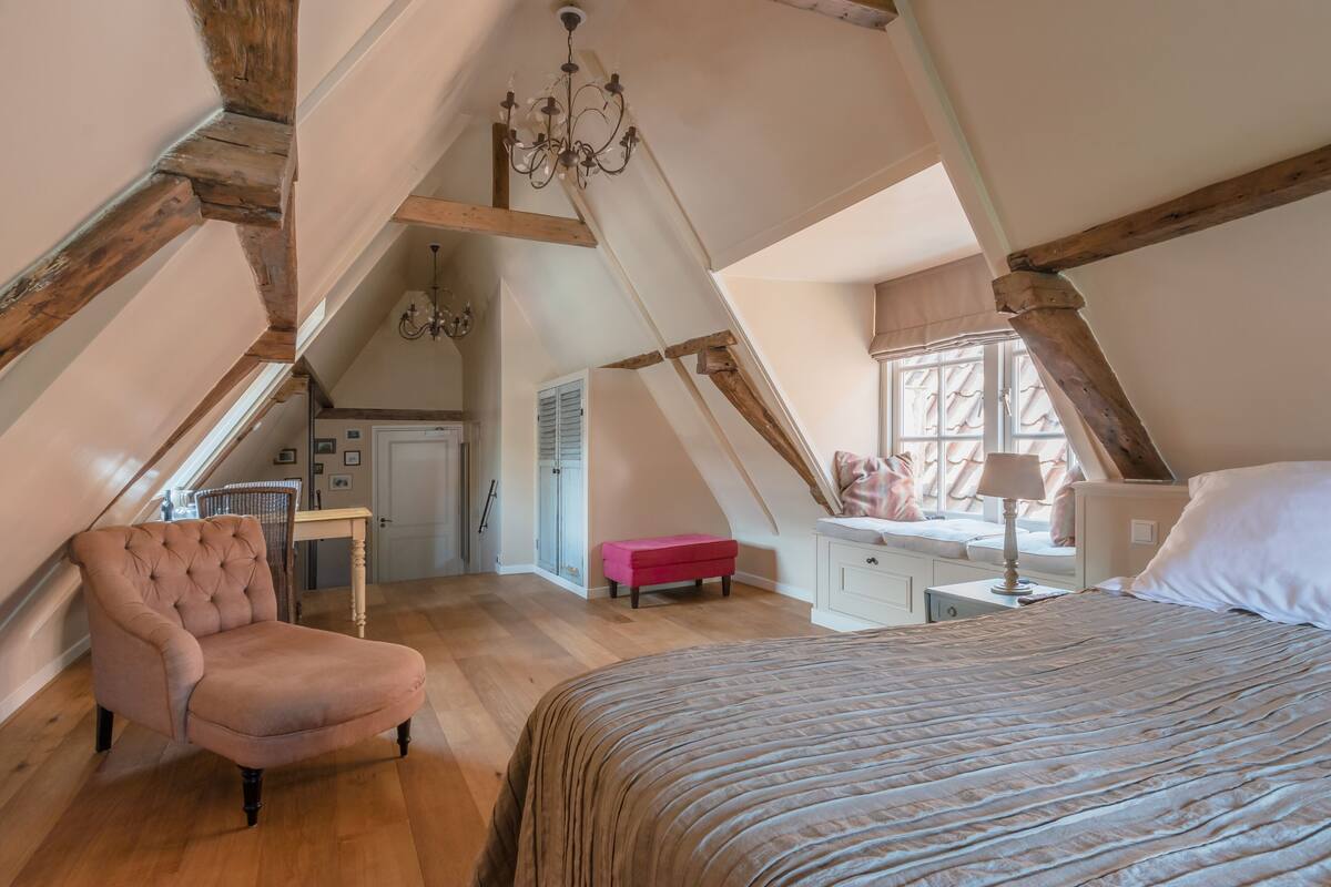 A bedroom with a bed, a chair, a desk, and a window with curtains.