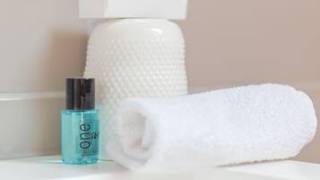 Un baño con una toalla blanca y una botella de gel para cabello y cuerpo sobre un estante blanco.