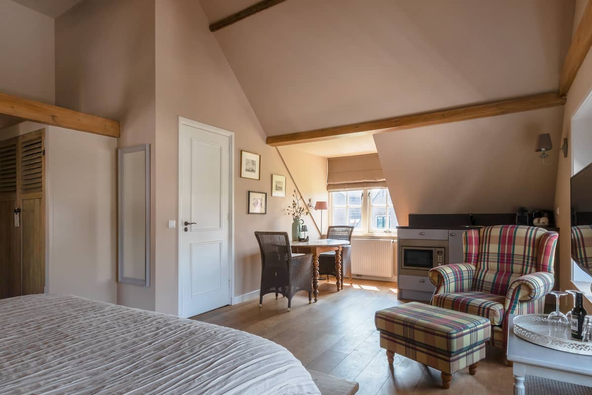 A bedroom with a large bed, a dining area with a table and chairs, a kitchen area, and a window with blinds.