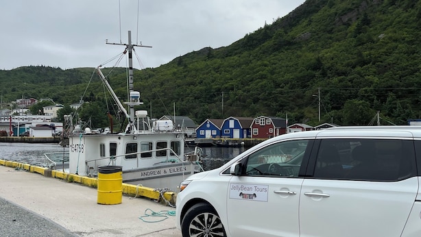 A white car parked by a dock with a boat in the background and a hill with greenery. - City Hostel-HI-ST.JOHN'S (St. John's)