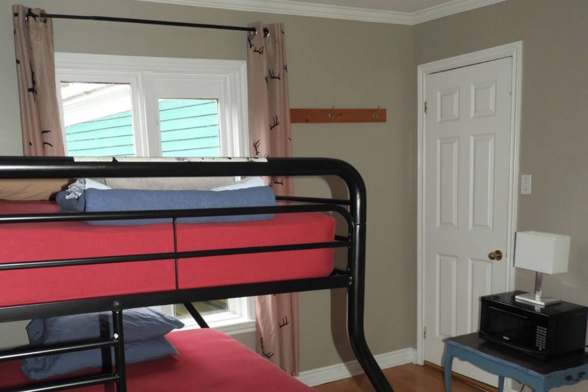 Een stapelbed met rode beddengoed, een tafeltje met een magnetron, en een deur in een kamer met houten vloeren.