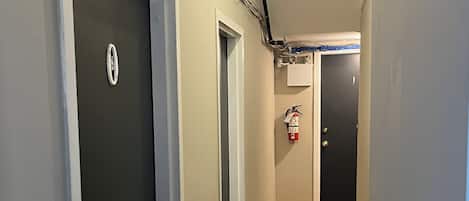 A hallway with wooden flooring, a fire alarm, and a door with a sign.