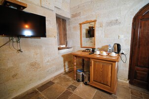 Una habitación con un armario de madera, un televisor montado en la pared, un espejo sobre el armario y una puerta a la derecha.