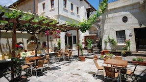 Un patio al aire libre con suelo de piedra, mesas y sillas de madera, y plantas en macetas.