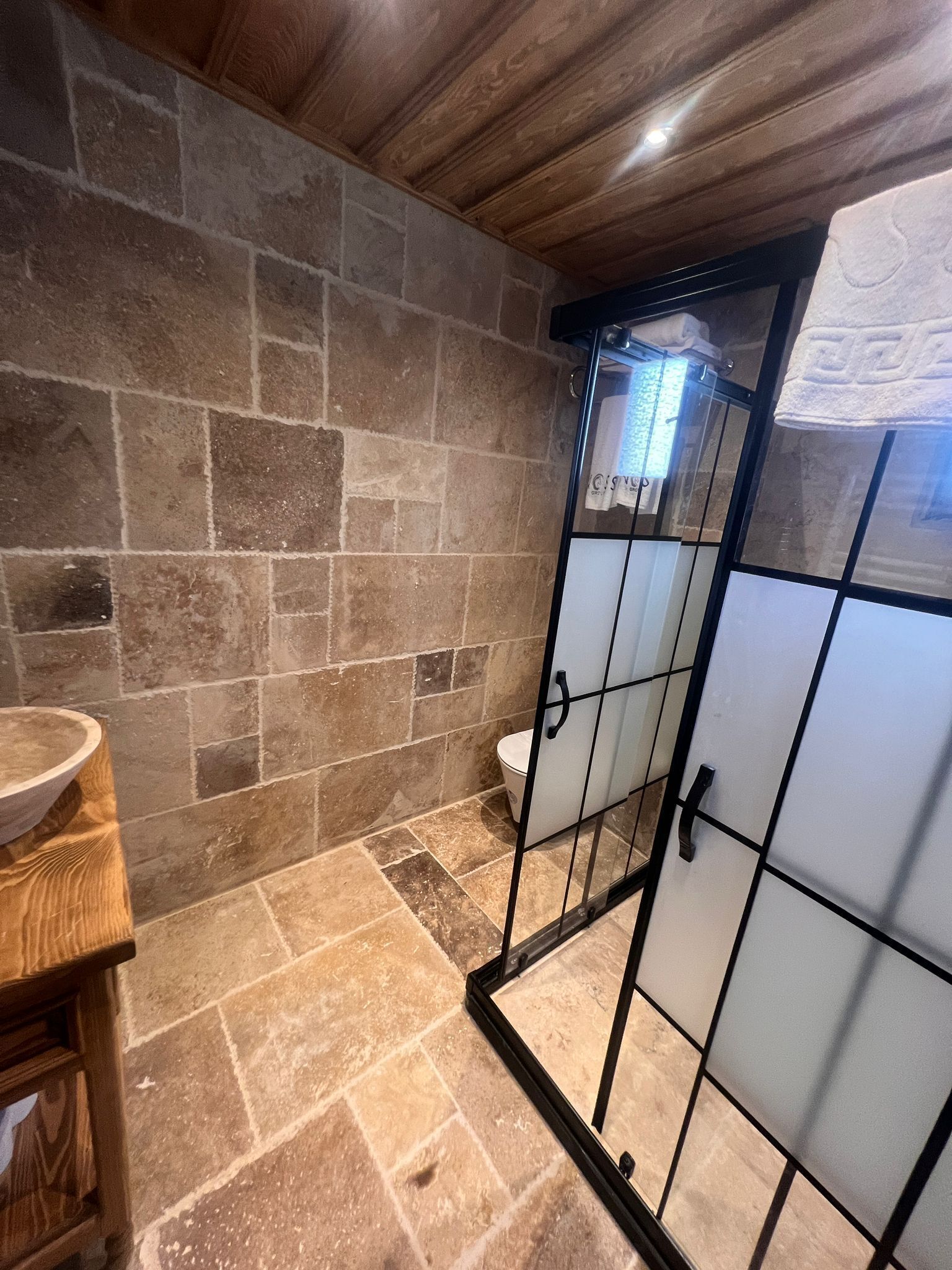 A bathroom with stone walls, a wooden vanity, and a glass shower enclosure.