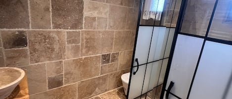 A bathroom with stone walls, a wooden vanity, and a glass shower enclosure.