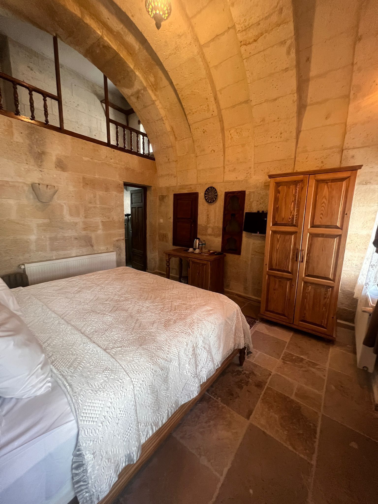 A bedroom with a large bed, wooden wardrobe, stone walls, and a sloped ceiling.
