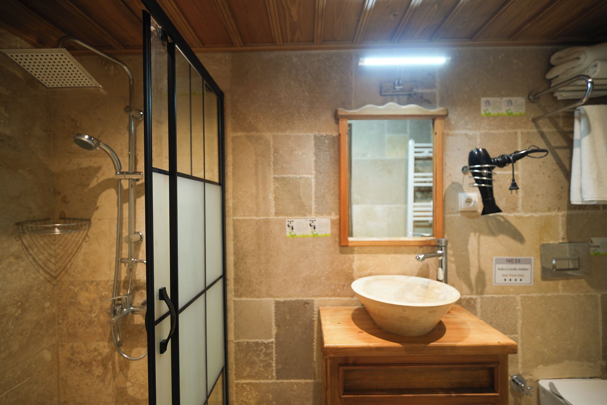Een badkamer met een houten wastafelmeubel, een ruime wastafel, een douche met handdouche, een handdoekhouder en een spiegel.