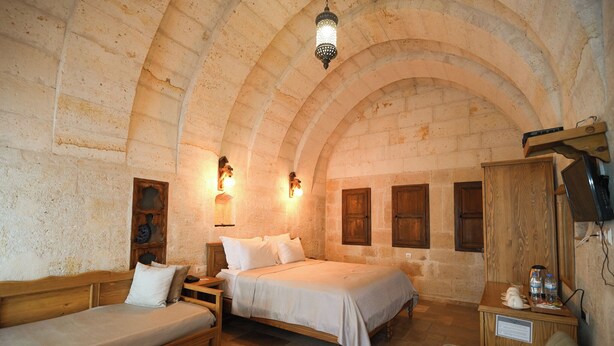 Una habitación con techo abovedado de piedra, dos camas, muebles de madera y luces fijadas a la pared.