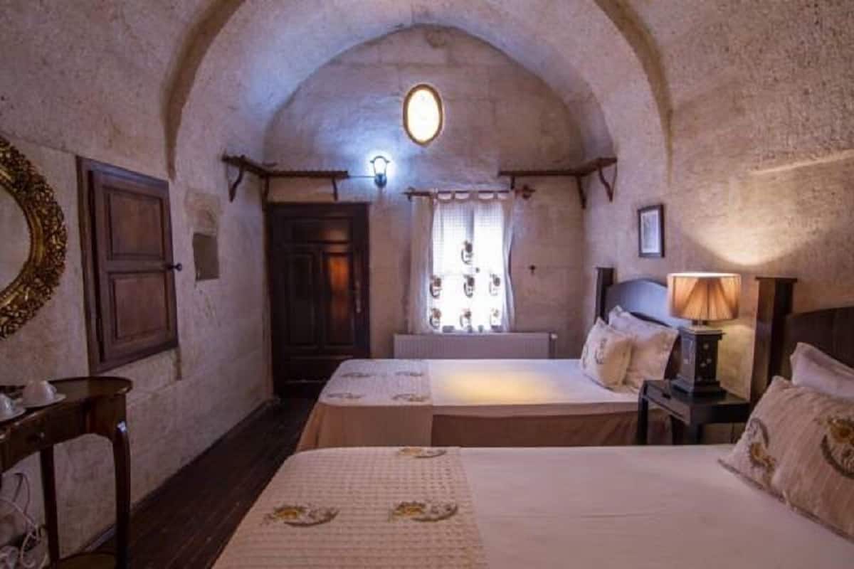 A room with two beds, a wooden door, a window with curtains, and a wall-mounted light fixture.